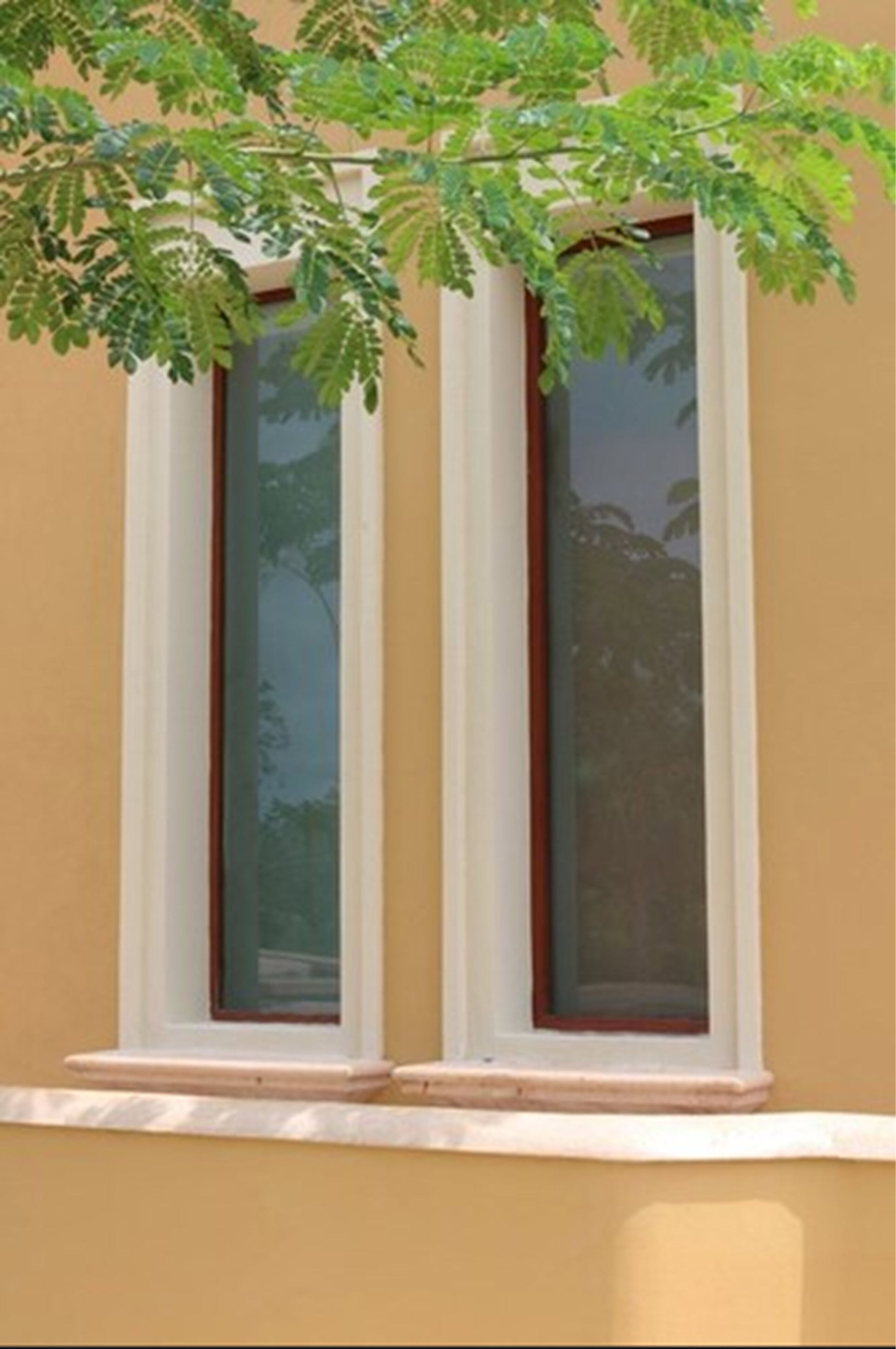 Una finestra con cornice bianca e davanzale marrone, incastonata in una parete beige.