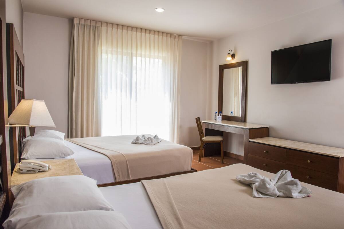 Habitación de hotel con dos camas, un escritorio, una silla, un televisor y un teléfono.