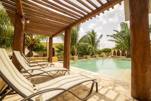 Zona de piscina con sillones de descanso y una pérgola de madera.