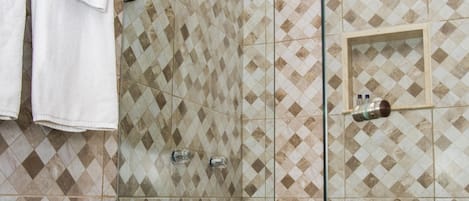 A glass-enclosed shower with a checkered tile pattern and a small shelf with toiletries.