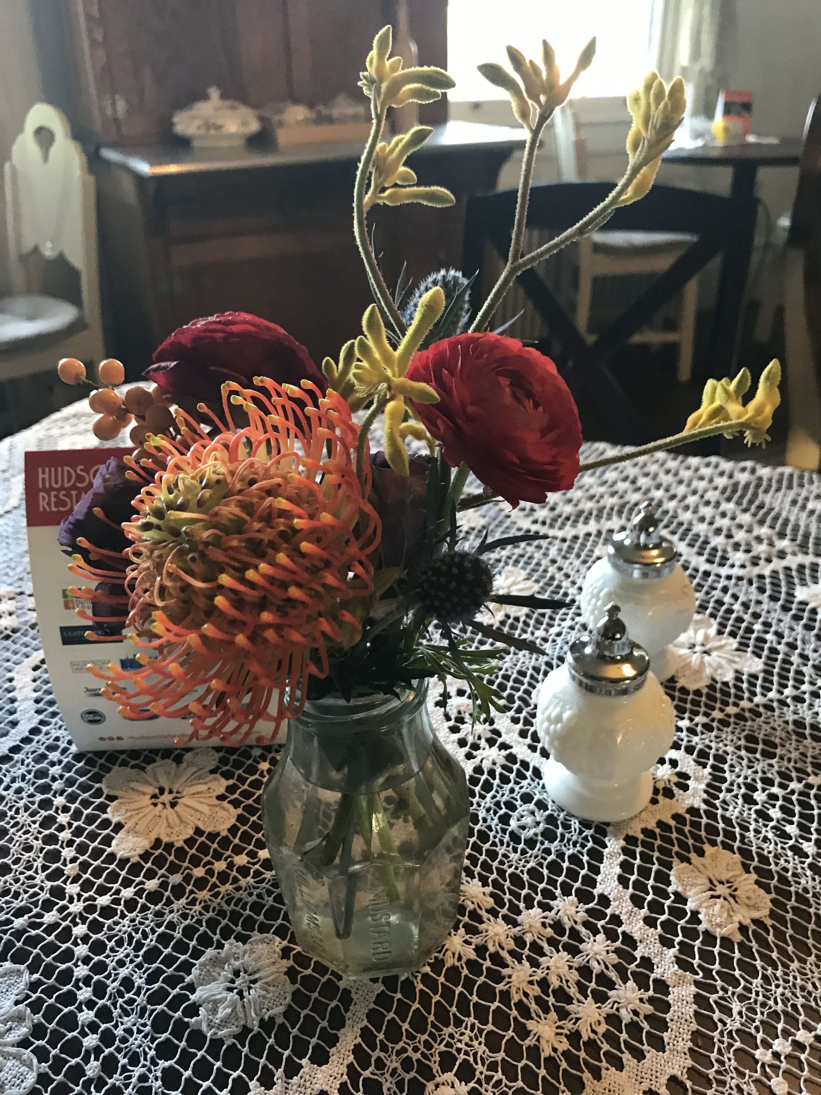 A glass vase with flowers on a lace tablecloth.