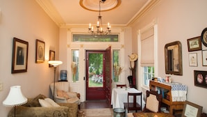 A cozy living room with a sofa, armchair, and a table with a vase. A chandelier hangs from the ceiling, and there are framed pictures on the walls. - Borland House Inn (Montgomery)