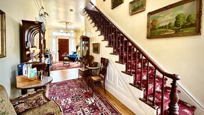 A grand hallway with a wooden staircase, a patterned carpet, and a dining area with chairs and a table. - Borland House Inn (Montgomery)