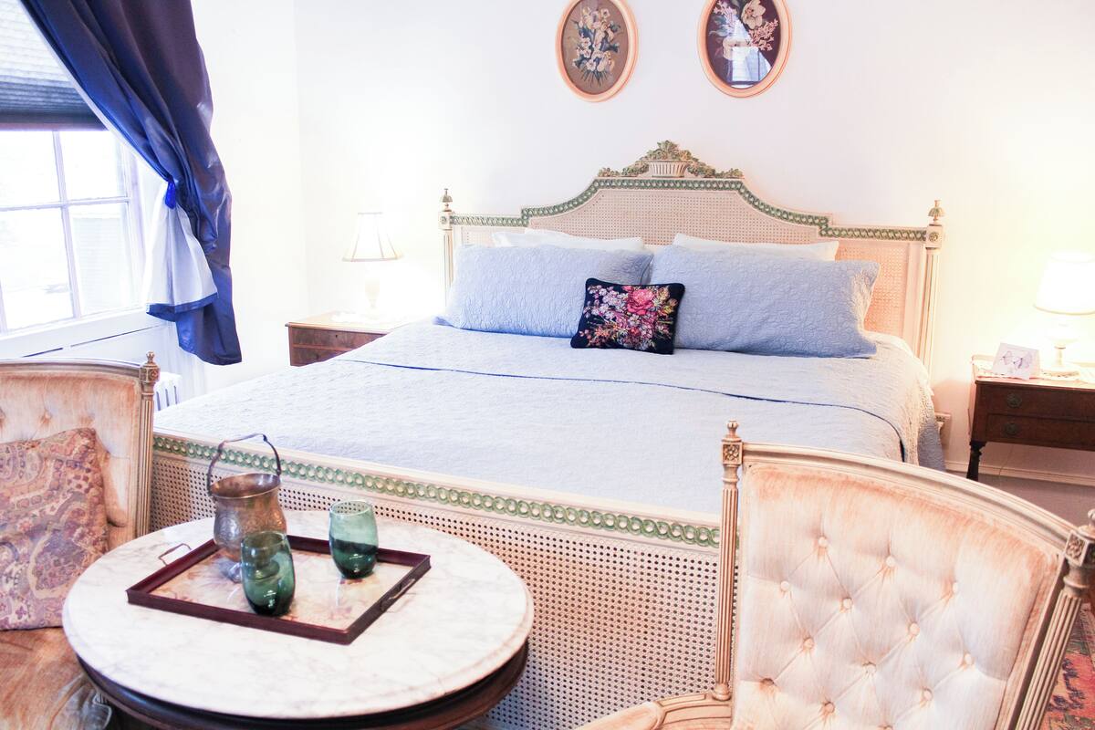 A bedroom with a large bed, two bedside tables, a round table with a tray, and a chair.