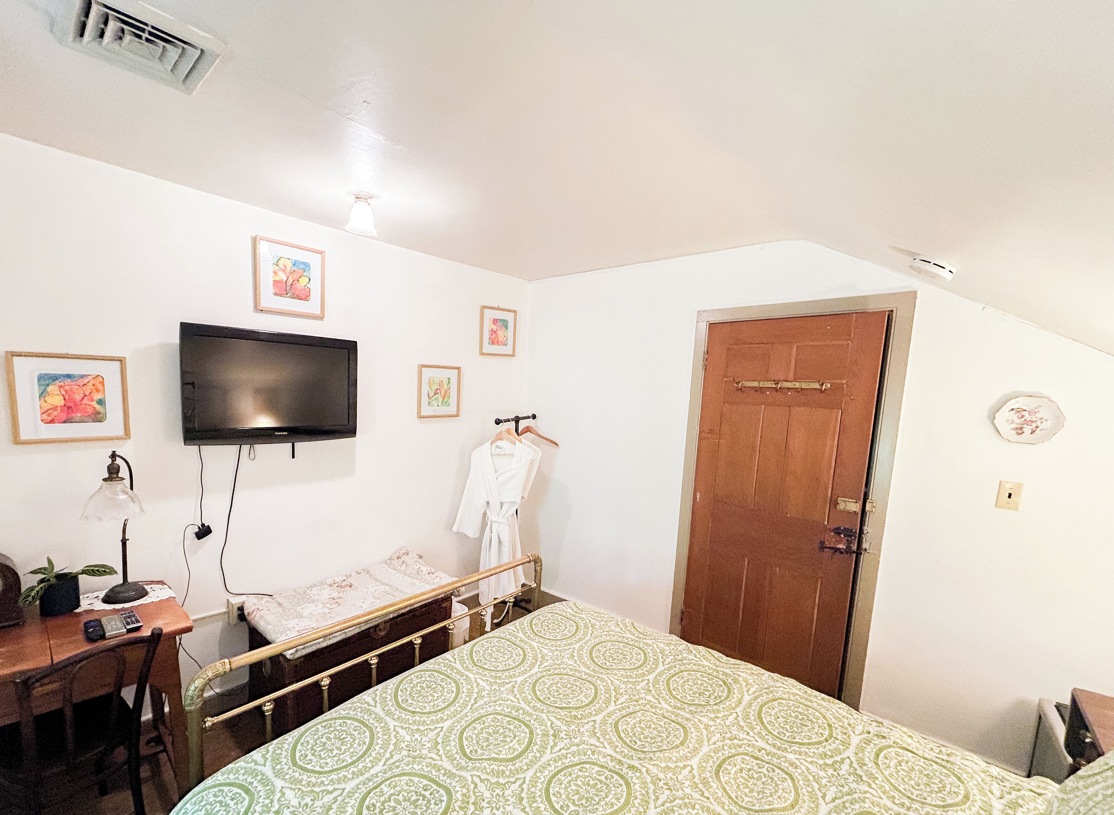A bedroom with a bed, a desk, a chair, a TV mounted on the wall, and a door.