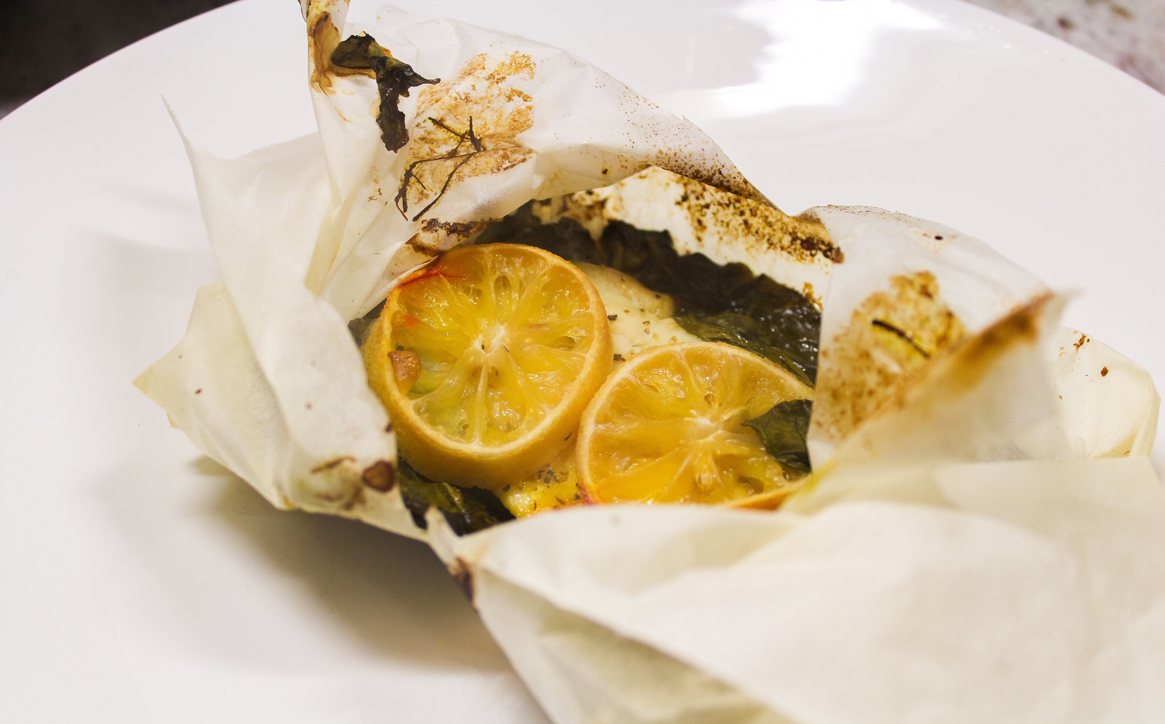 En tallerken med en madvare pakket ind i papir, muligvis med skiver af citrusfrugter.
