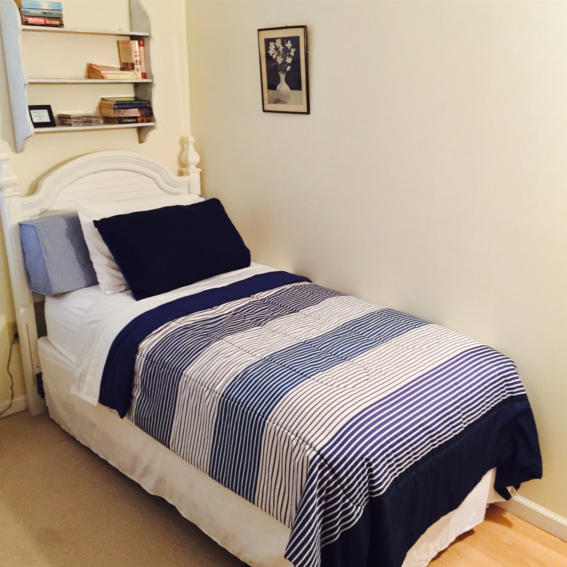A neatly made bed with a striped bedspread, a white headboard, and a bedside table with a lamp.