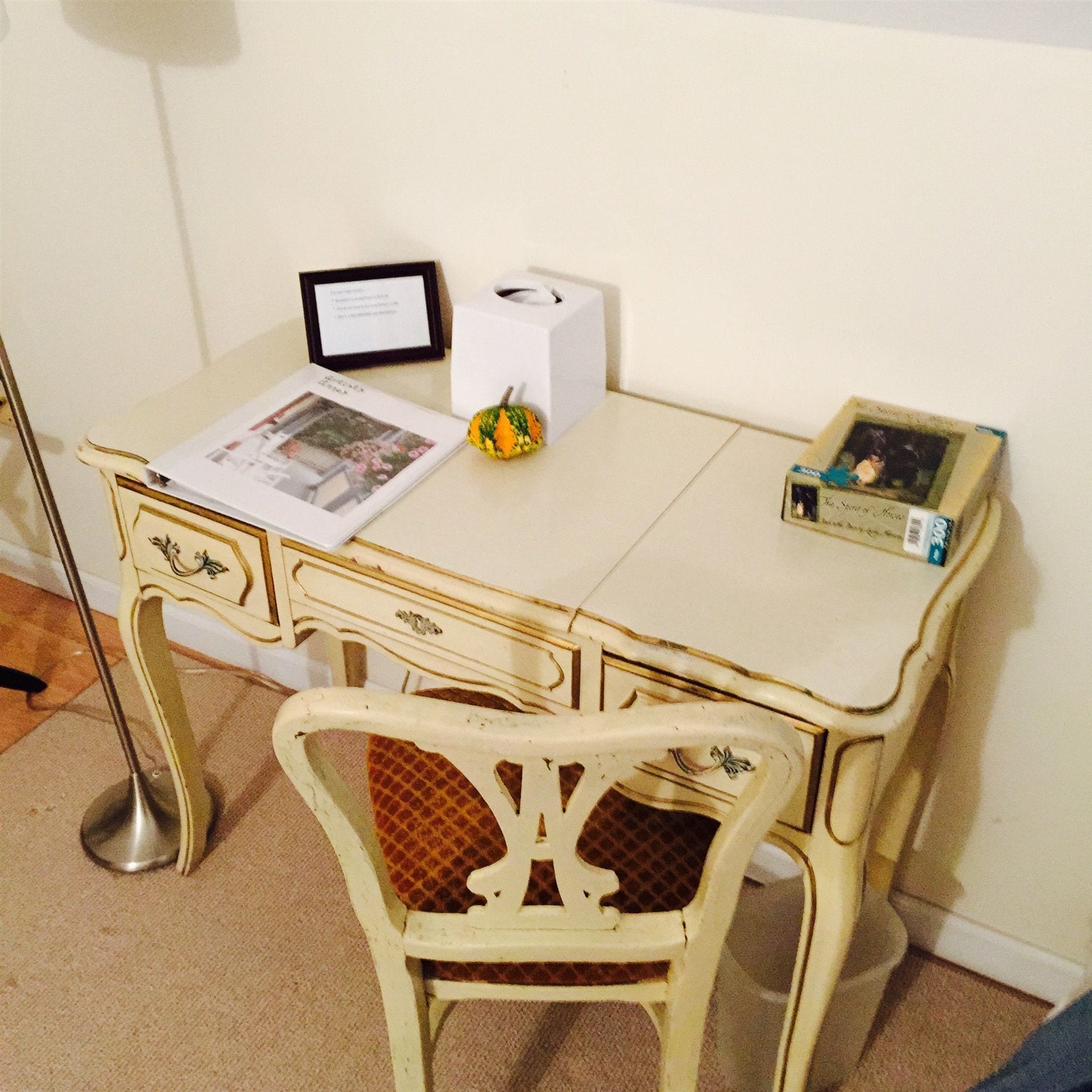 A vintage-style desk with a chair, a framed certificate, a tissue box, and a small decorative pumpkin.