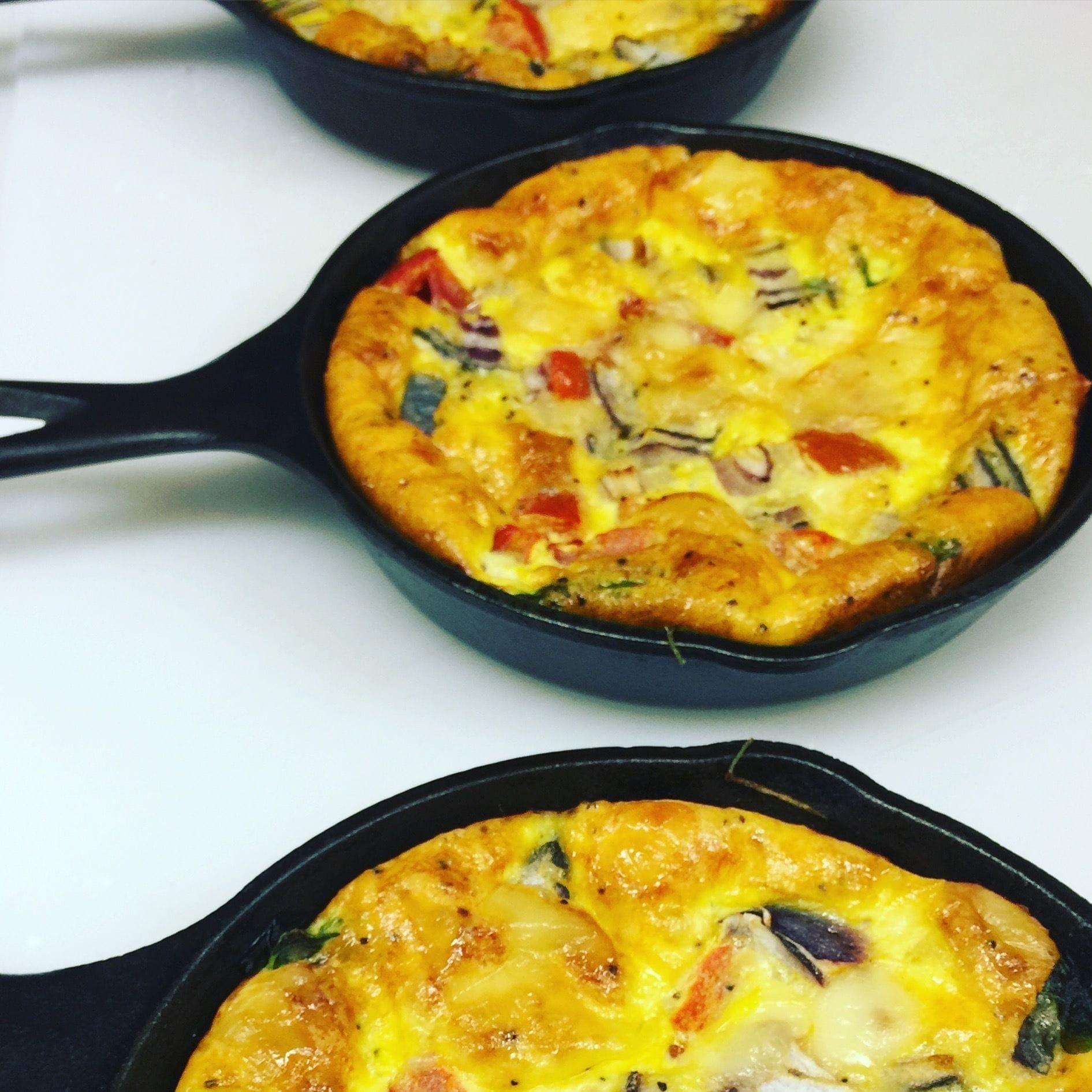 Three cast iron skillets filled with a baked dish, likely a frittata, on a white surface.