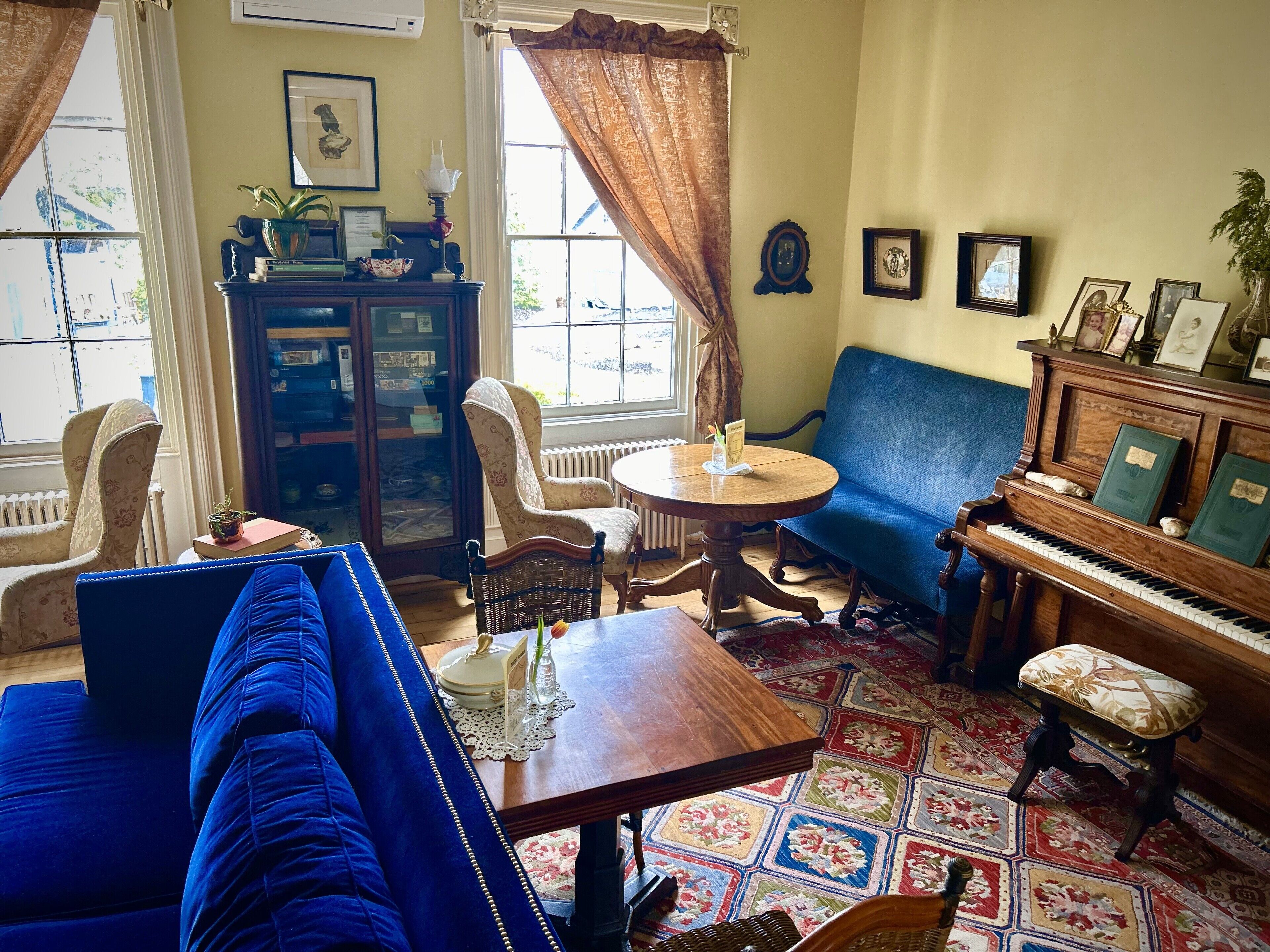 A cozy living room with a blue sofa, a wooden piano, and a patterned rug.