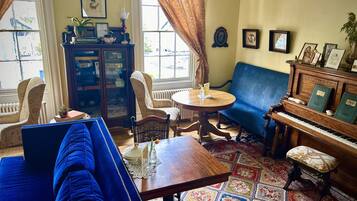 A cozy living room with a blue sofa, a wooden piano, and a patterned rug.