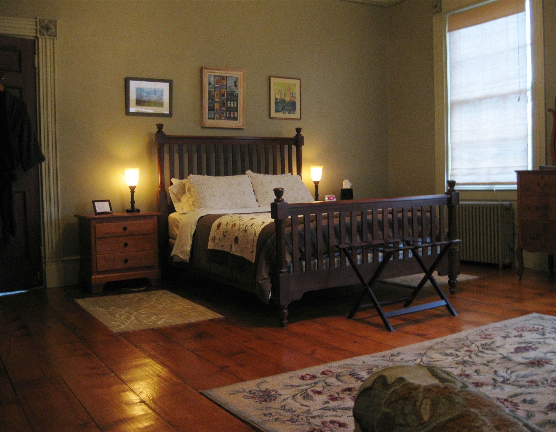 Une chambre à coucher avec un lit en bois, deux tables de chevet avec des lampes, un radiateur et une fenêtre avec des stores.