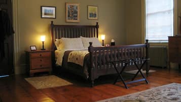 Une chambre à coucher avec un lit en bois, deux tables de chevet avec des lampes, un radiateur et une fenêtre avec des stores.