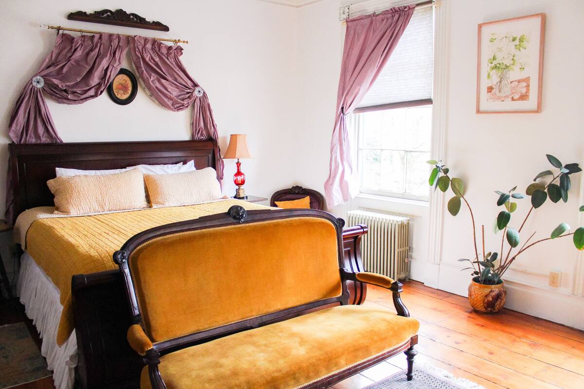 A bedroom with a bed, a chair, a radiator, and a potted plant.