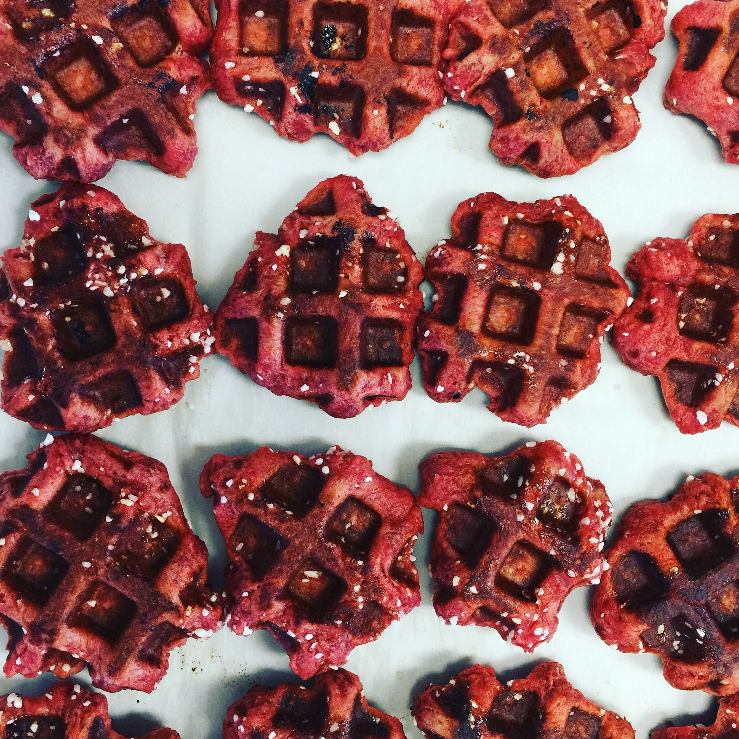 A close-up of red, waffle-shaped food items with sesame seeds on a white surface.