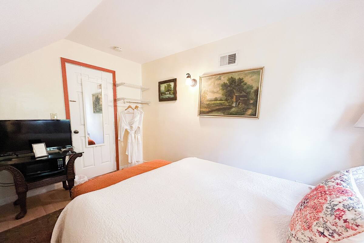 A hotel room with a bed, a television, a wardrobe, and two framed pictures on the wall.