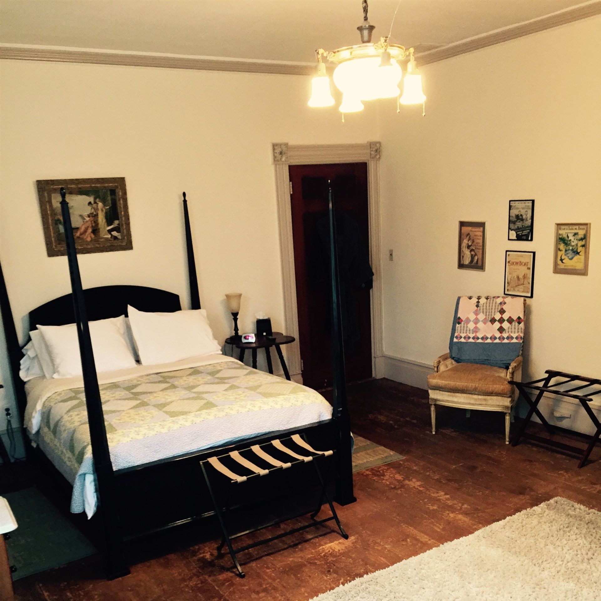 A bedroom with a four-poster bed, a small table with a lamp, a chair, and a white rug.