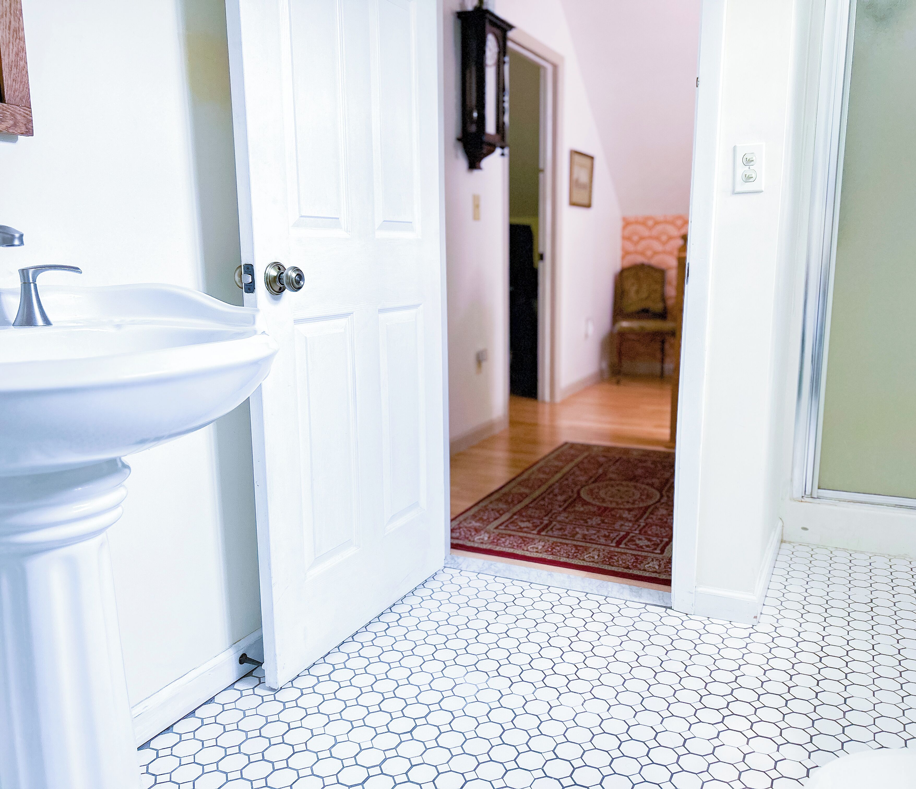 A bathroom with a white sink and a door leading to a hallway with a patterned floor.