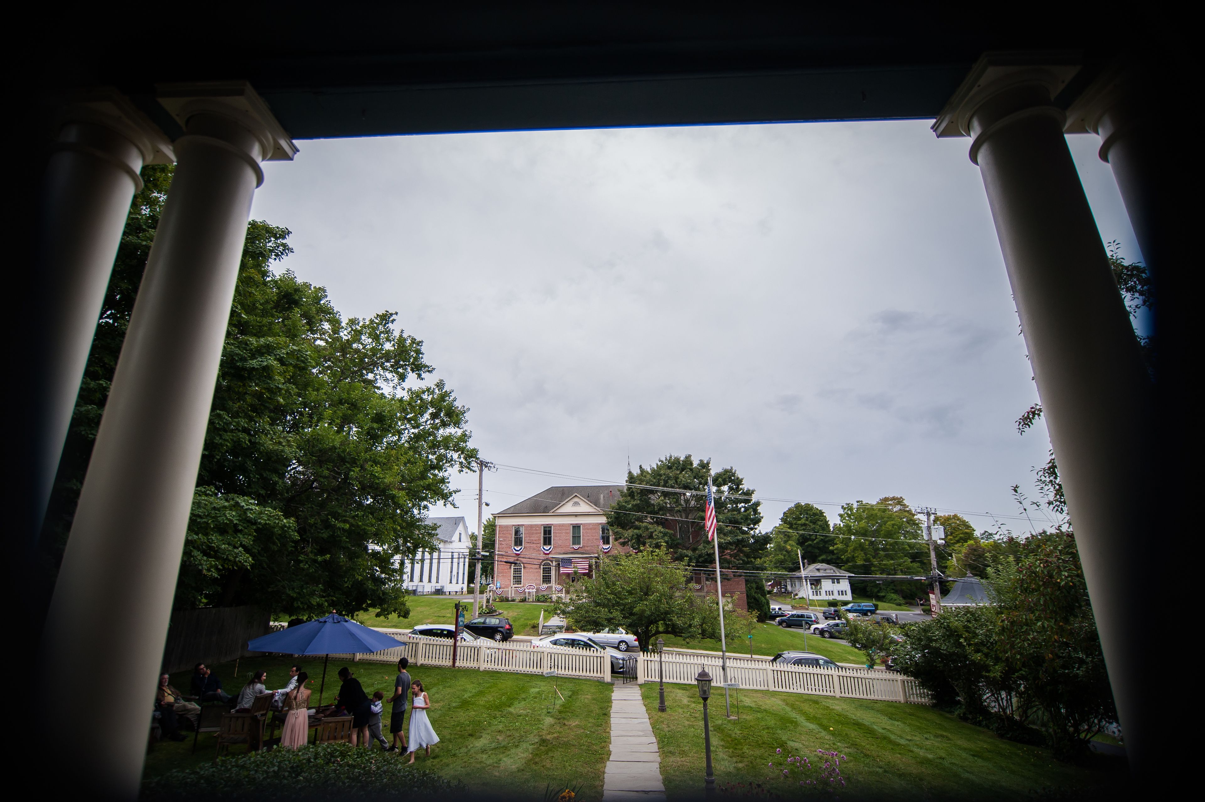 A view of a building with columns, a lawn, and a fence.