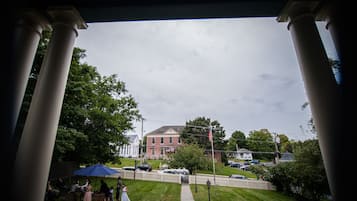 A view of a building with columns, a lawn, and a fence.
