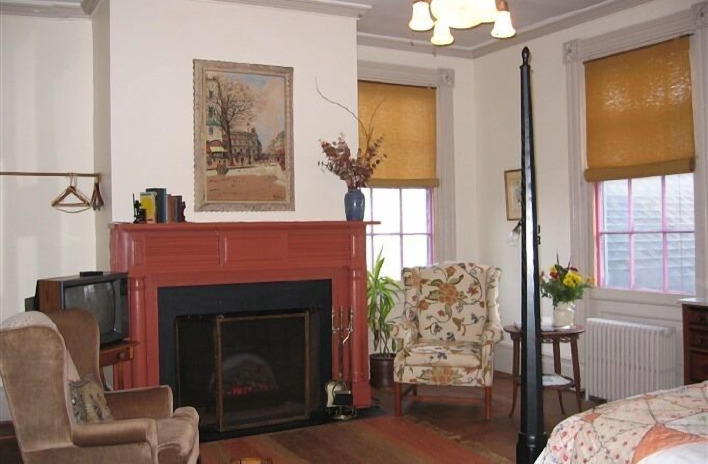 A living room with a fireplace, a television, a floral armchair, and a painting on the wall.