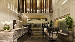 Een moderne hotellobby met een marmeren receptiebalie, een zithoek en een grote potplant.