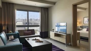 Une chambre d’hôtel moderne dotée d’une grande fenêtre, d’un canapé, d’une table basse, d’un téléviseur, d’un bureau et d’un lit.