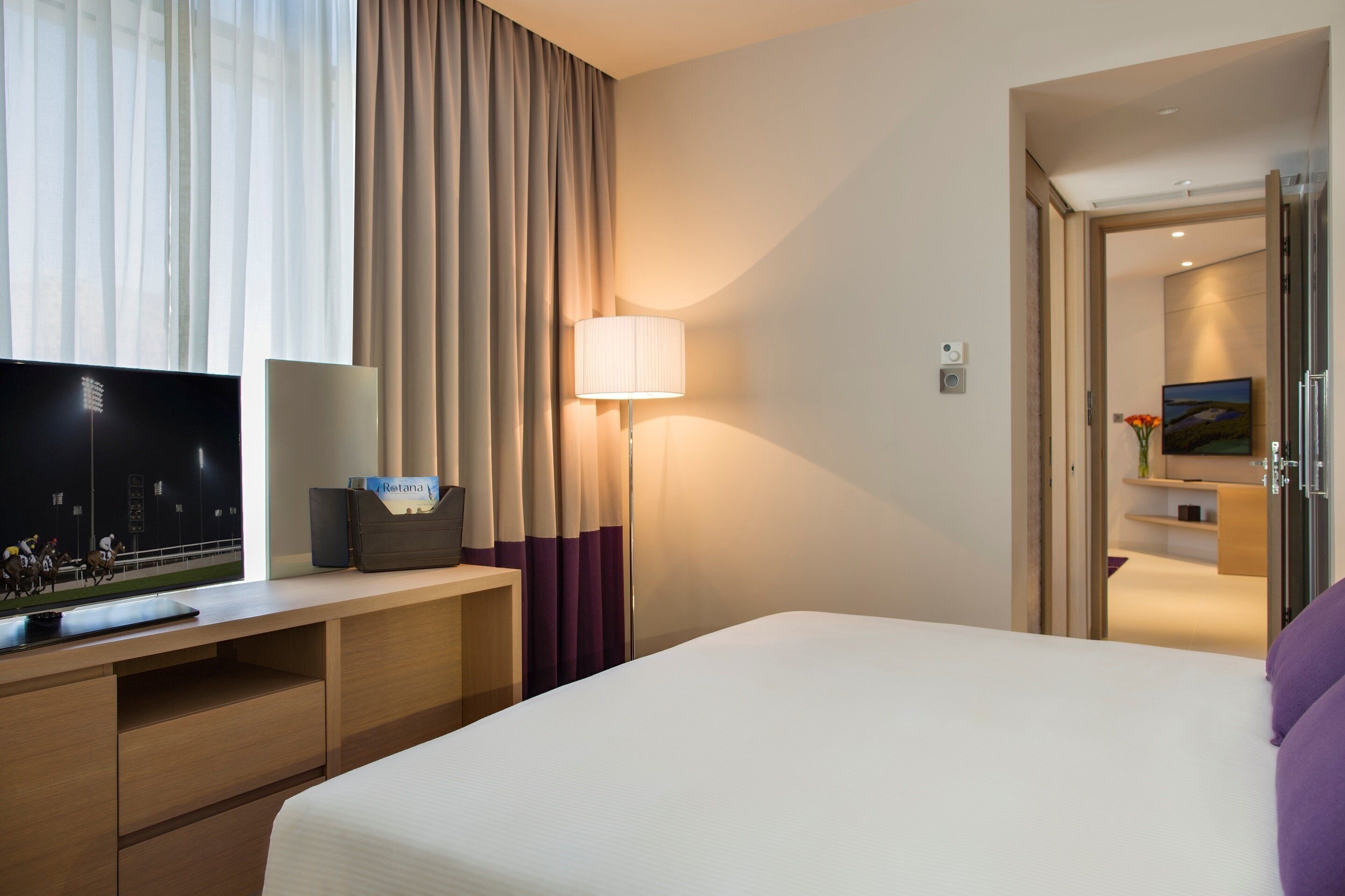 Een hotelkamer met een bed, een bureau met een computer, een lamp en een televisie.