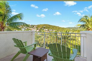 A balcony with two green Adirondack chairs, a small table, and a view of a hillside town. - Margaritaville Vacation Club - St. Thomas (St. Thomas)