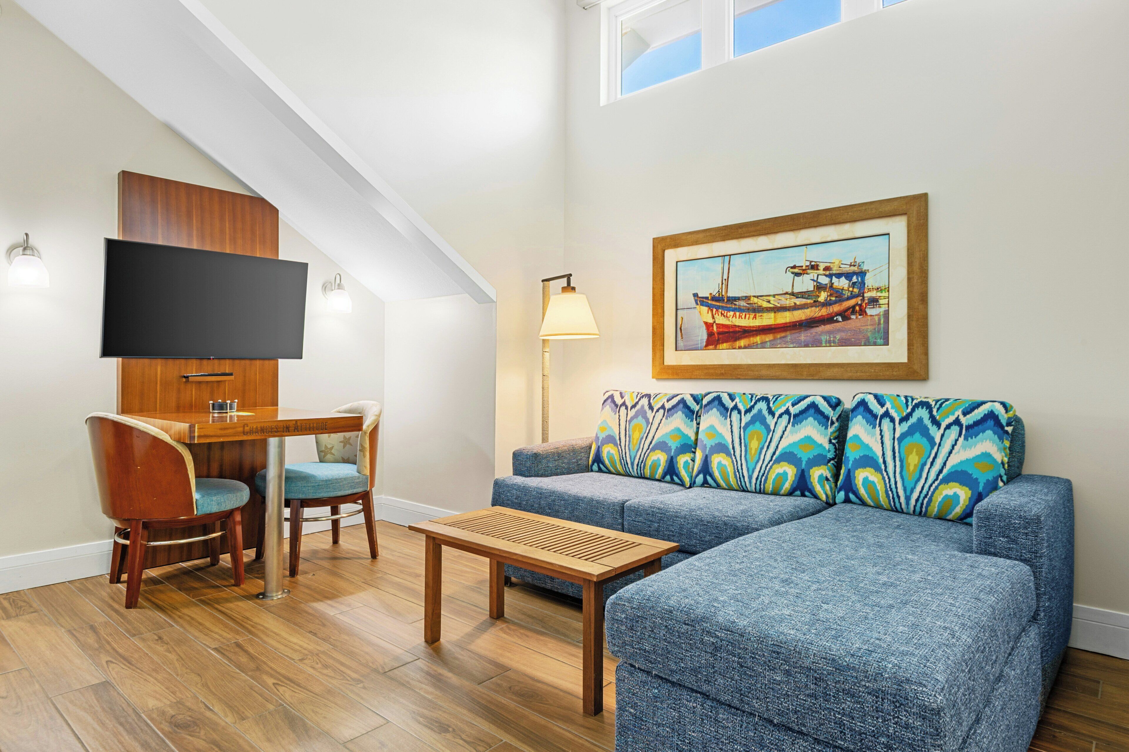 A modern living room with a flat-screen TV, a wooden desk, a blue sofa, and a framed picture of a boat.