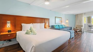 A hotel room with a large bed, a wooden headboard, a ceiling fan, a nightstand with a phone, a seating area with a sofa and armchairs, and a view through a glass door. - Margaritaville Vacation Club - St. Thomas (St. Thomas)