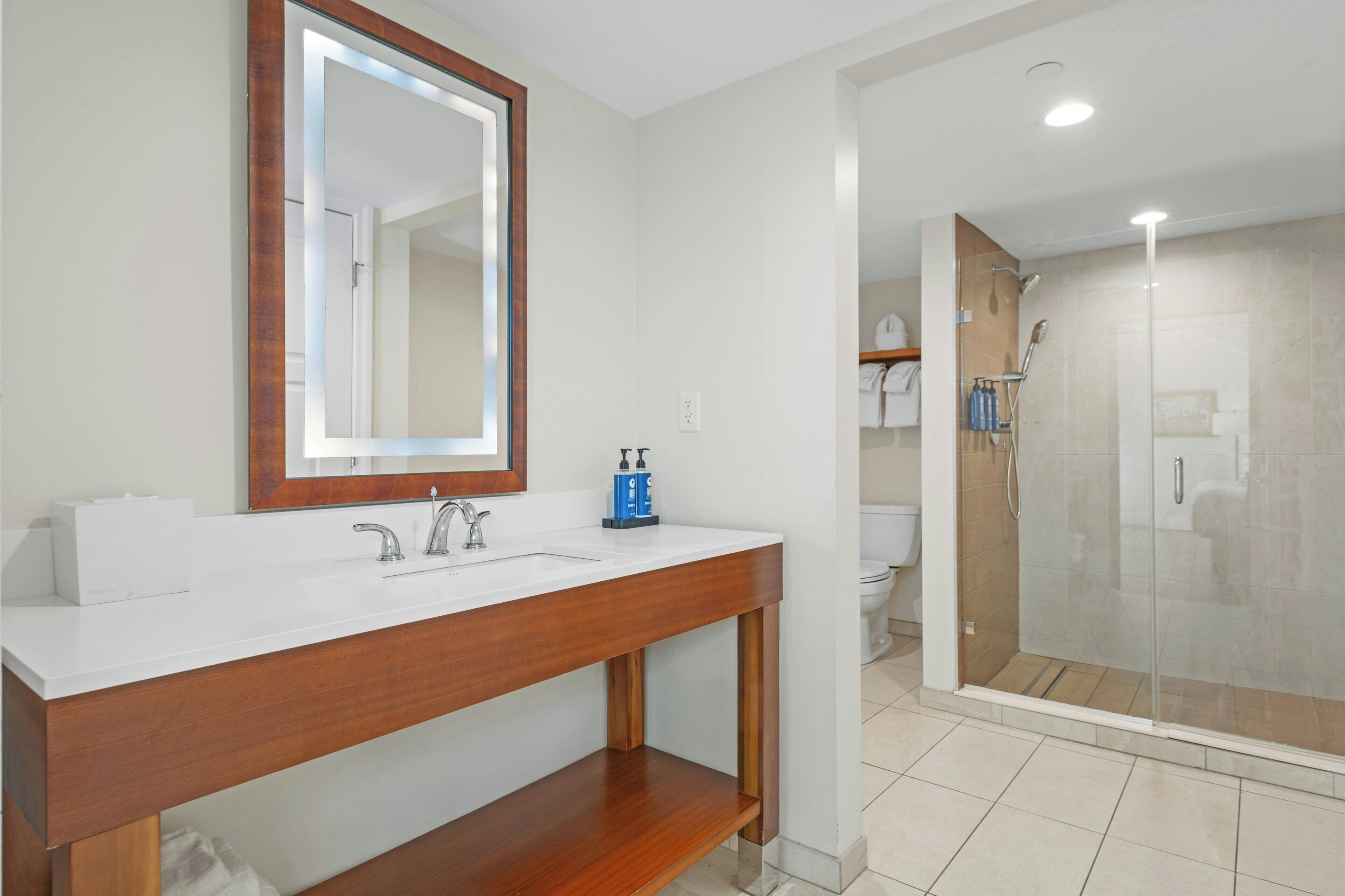 A bathroom with a wooden vanity, a large mirror, a shower area, and a toilet.
