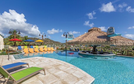 A swimming pool with lounge chairs and umbrellas, a thatched-roof structure, and a sign for 'Chill Beach'.