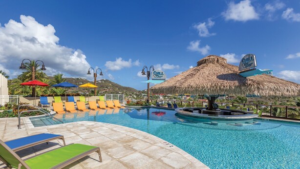 A swimming pool with lounge chairs and umbrellas, a thatched-roof structure, and a sign for 'Chill Beach'.