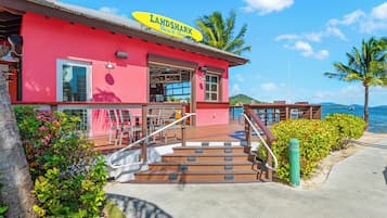 Een strandbar genaamd 'LANDSHARK' met een rode gevel, terras en uitzicht op zee.