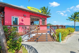 A beach bar named 'LANDSHARK' with a red exterior, outdoor seating, and a view of the sea.