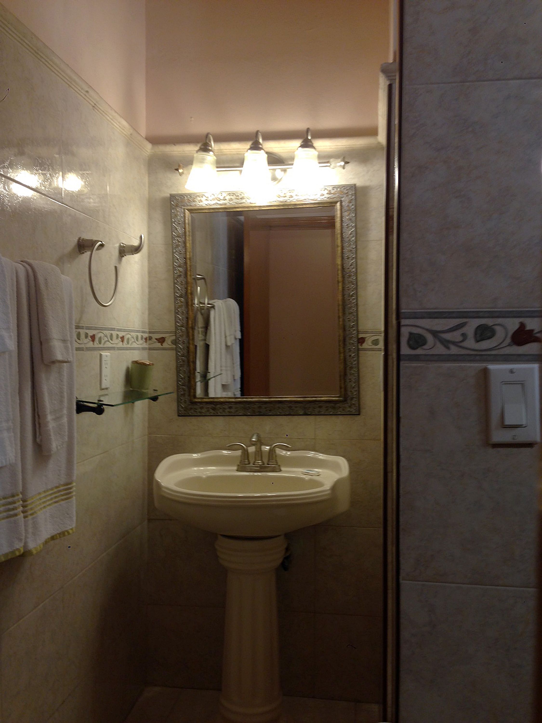 Ein Badezimmer mit einem Standwaschbecken, einem beleuchteten Spiegel und einem Handtuchhalter.