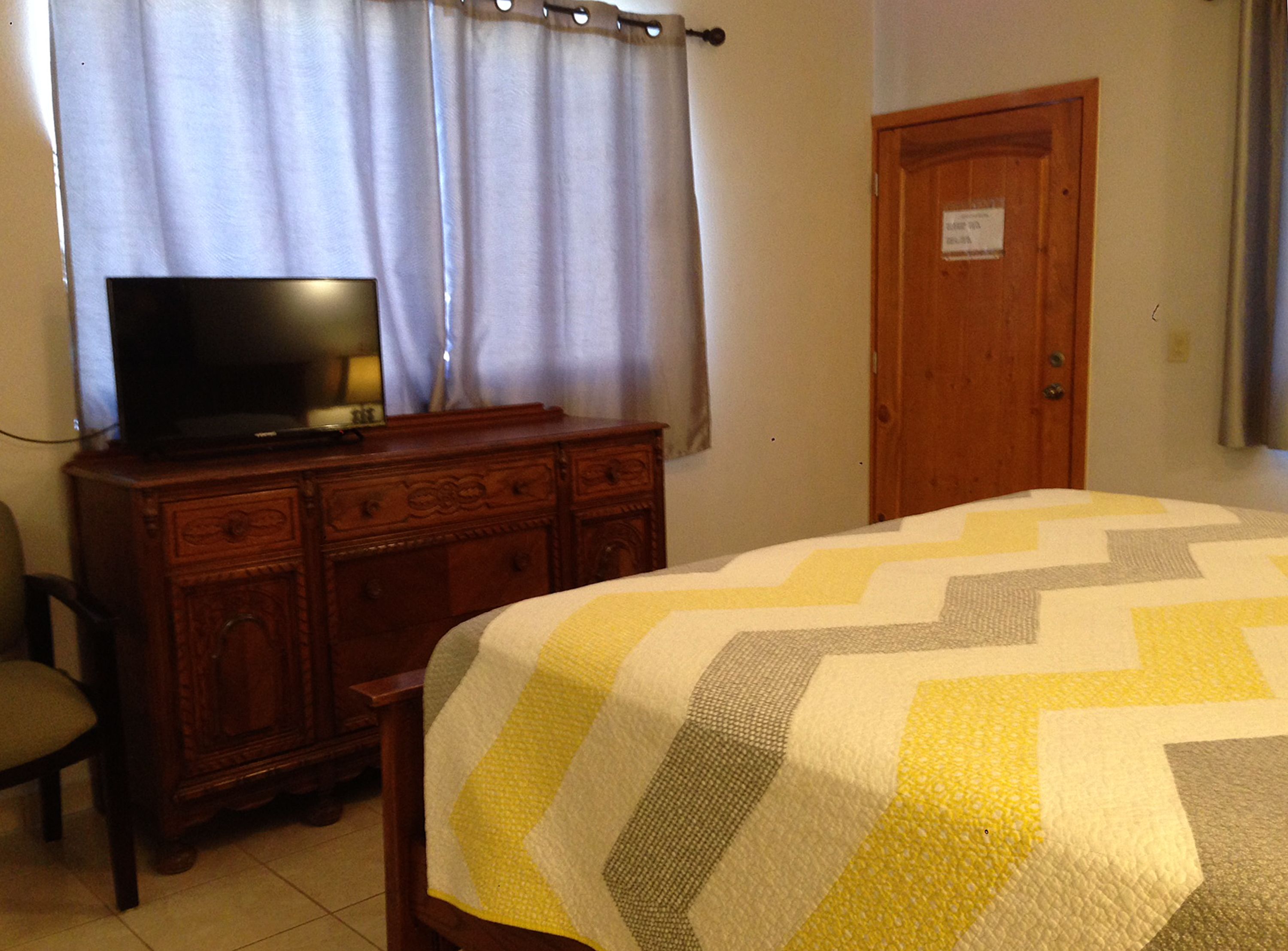 Un dormitorio con una cama, un aparador de madera, un televisor encima del aparador y una puerta con un cartel.