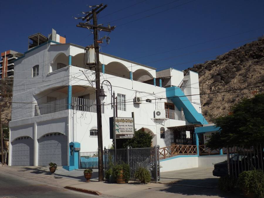 Un hotel de varios pisos con balcones, una pared azul de acento y una entrada protegida por una reja.