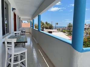 Un balcone con pavimento piastrellato, un tavolo con sedie e vista sul mare e sugli edifici.