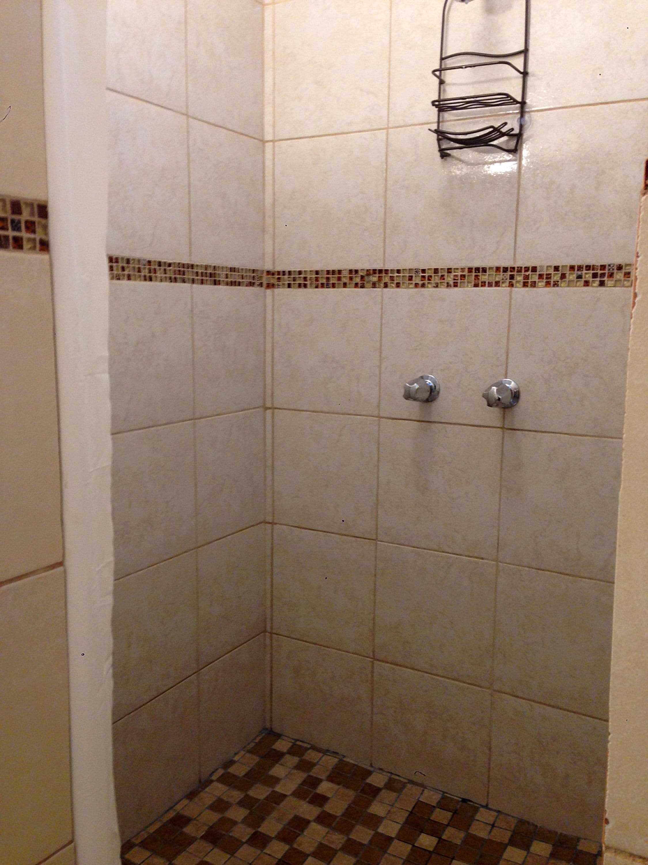 A shower area with tiled walls and floor, a metal shower head, and a towel rack.