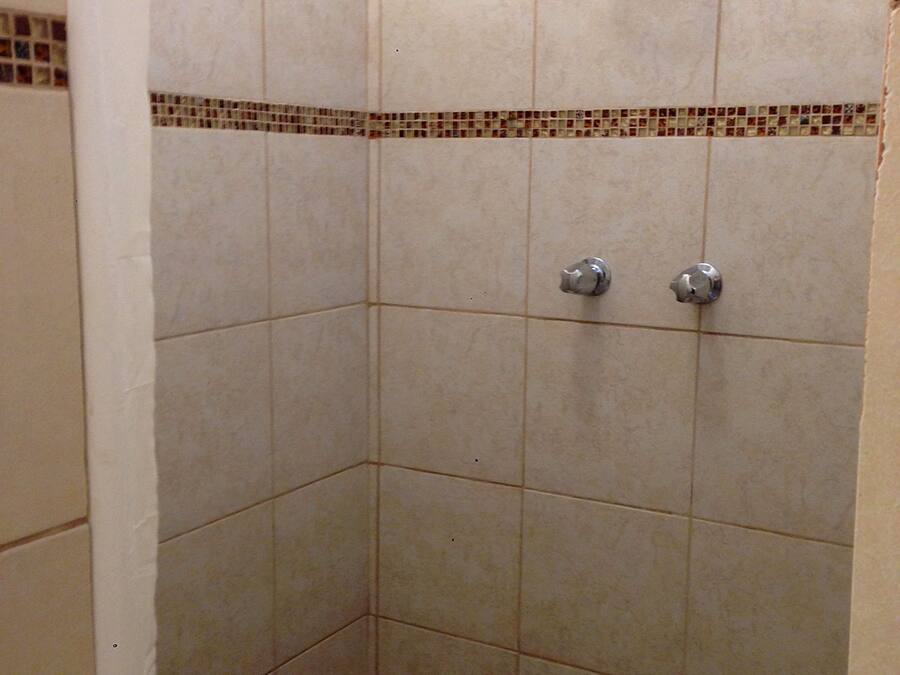 A shower area with tiled walls and floor, a metal shower head, and a towel rack.