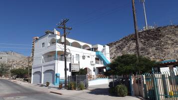 A multi-story building with balconies, a gated entrance, and a mountainous backdrop.