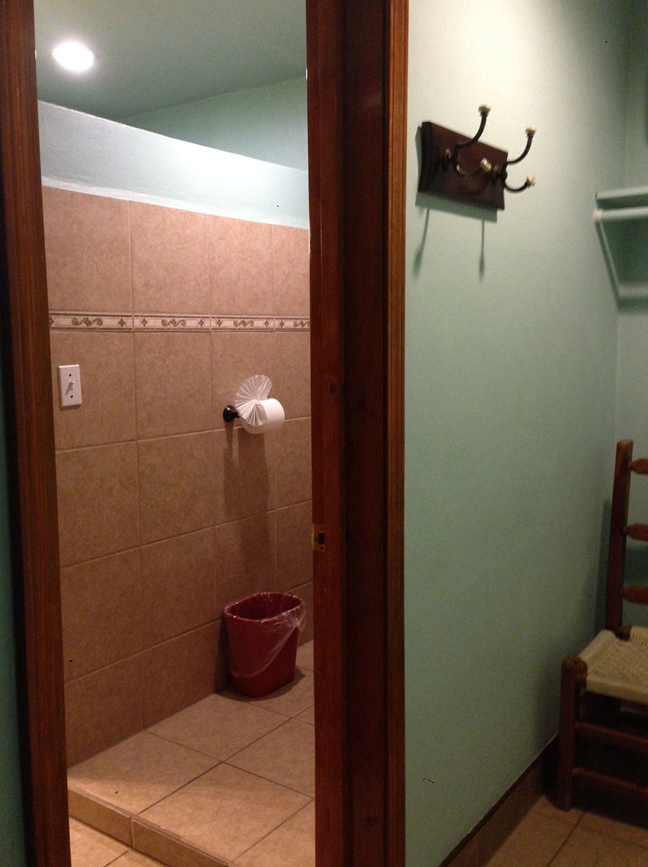 Un baño con ducha, un cubo rojo y un perchero en la pared.