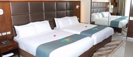 A hotel room with a large bed, a bedside table, a mirror, and a carpeted floor.
