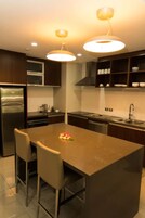 Une cuisine moderne dotée d’un îlot central, d’appareils électrom énagers en acier inoxydable et de luminaires suspendus.