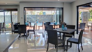 A modern indoor dining area with glass walls, wicker furniture, and a view of the ocean. - The Palms Denarau Fiji (Nadi)