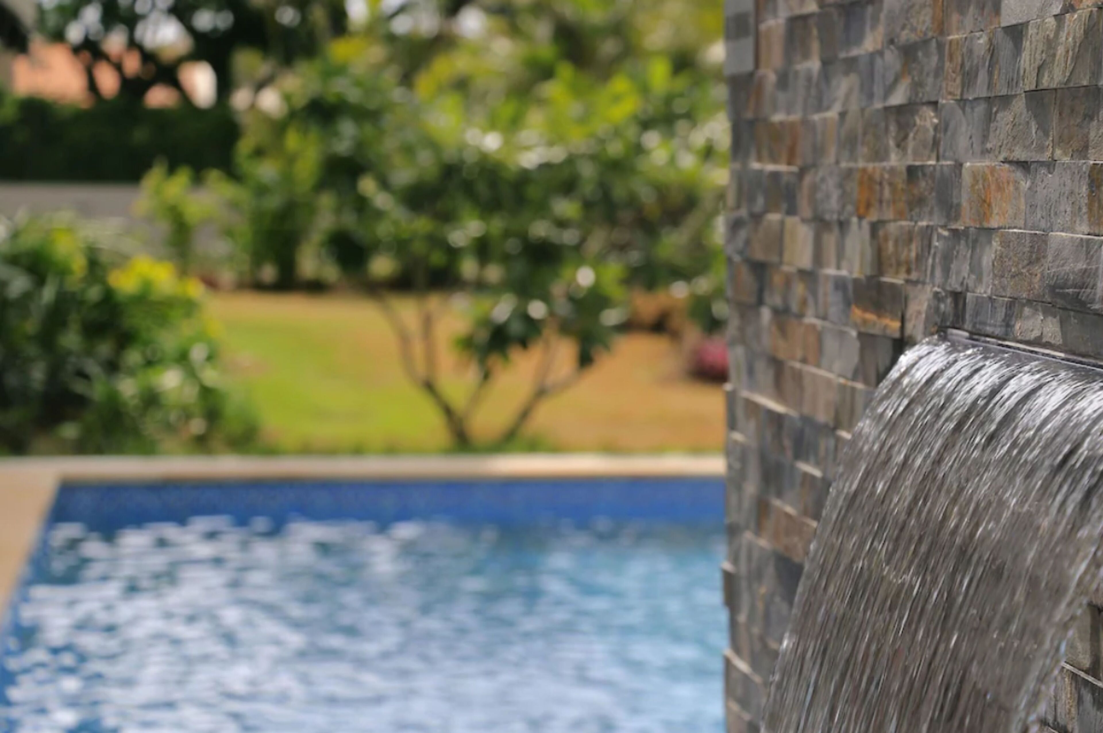 A pool with a waterfall feature and a stone wall.