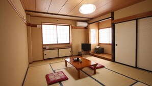 Una habitación japonesa tradicional con suelo de tatami, una mesa de madera, un televisor y puertas correderas.