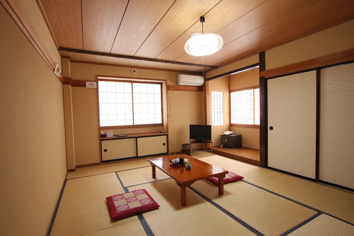 Ein traditioneller japanischer Raum mit Tatami-Böden, einem Holztisch, einem Fernseher und Schiebetüren.